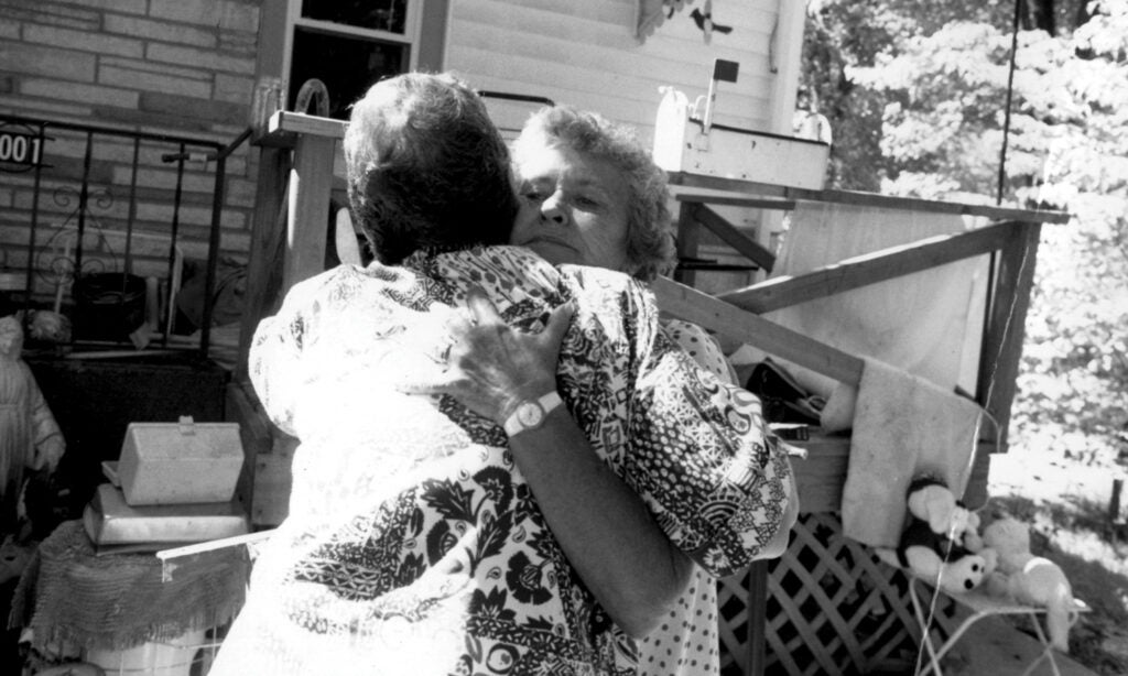 Two women hug each other in front of an old house.