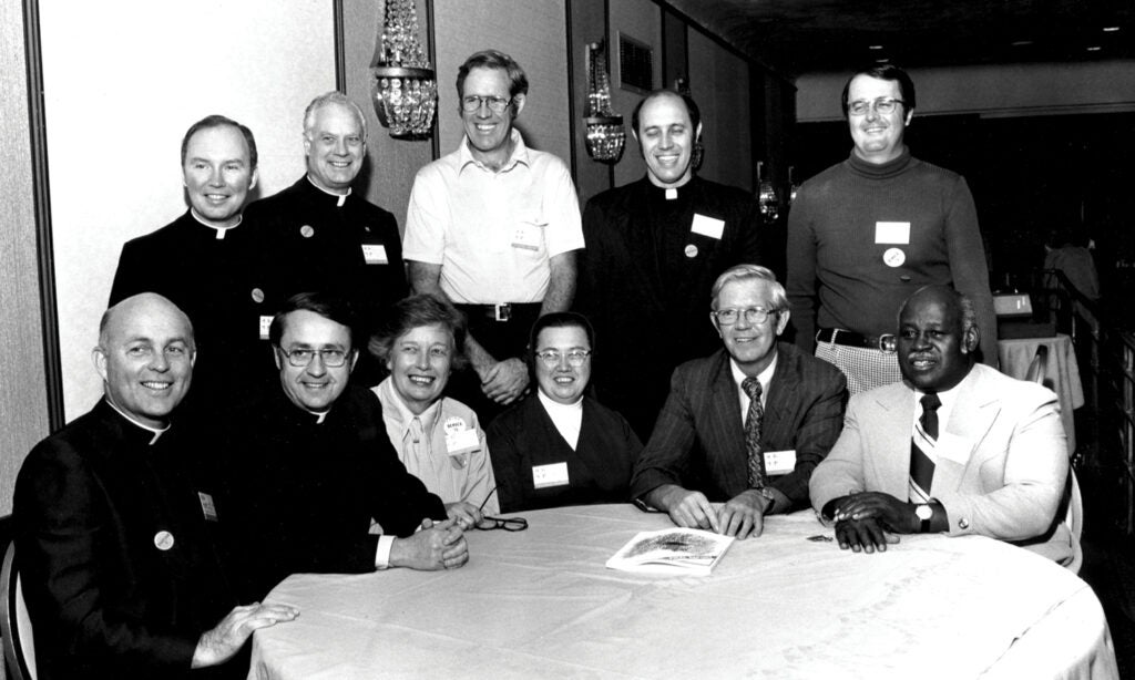 The authors of the Cadre Study gather around a table in this black and white photo. There are 11 people in the photo, half of them priests or nuns.