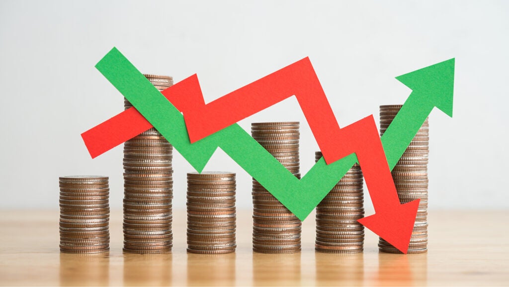 A stock image of six stacks of coins, each of varying height, with a red arrow and green, going up and down as if on a graph.